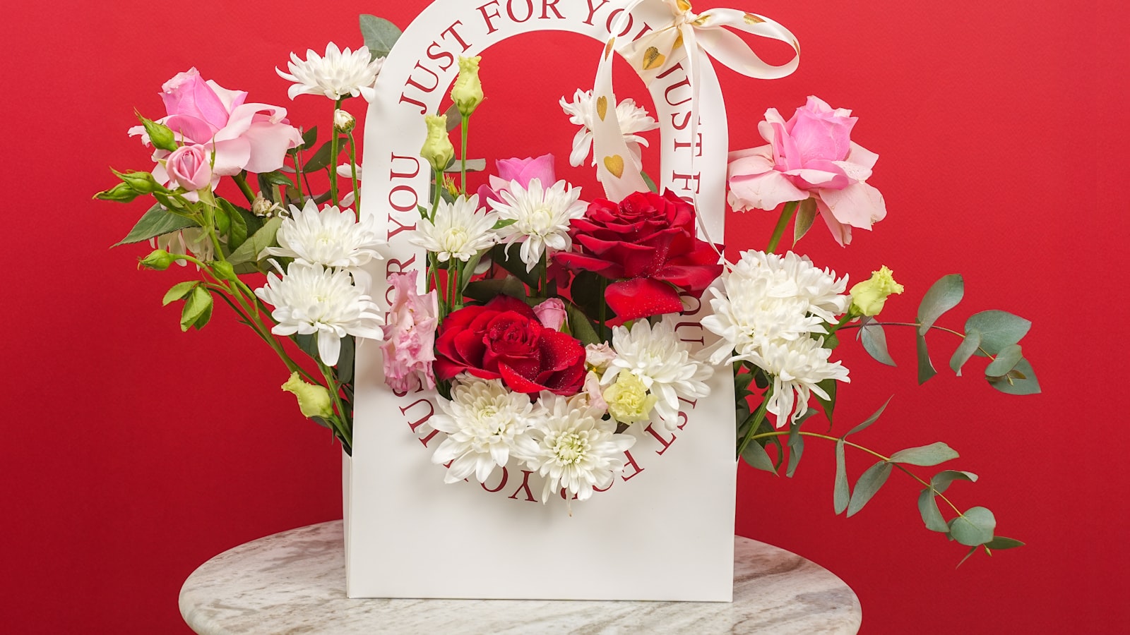 A floral arrangement in a white bag with red background