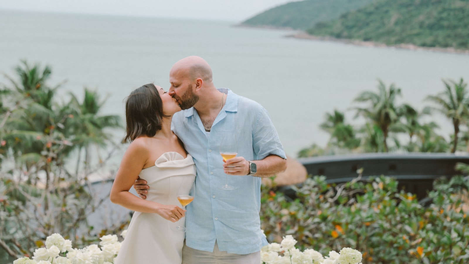 Couple kissing with drinks by the ocean.