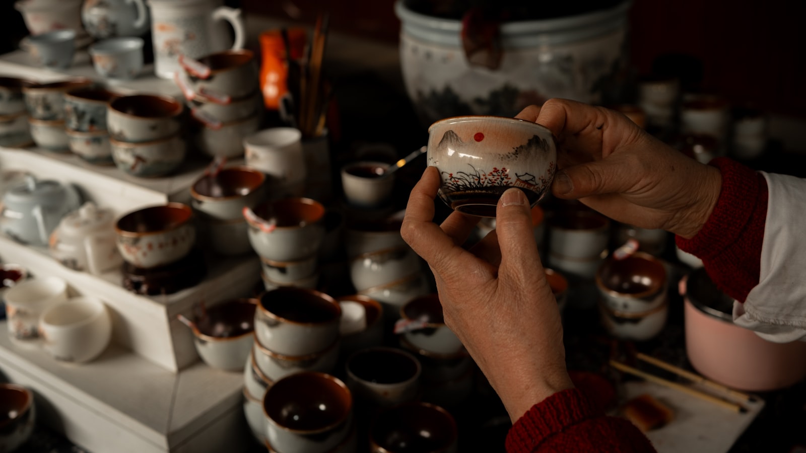 Hands holding a small decorative cup amidst many ceramic cups.