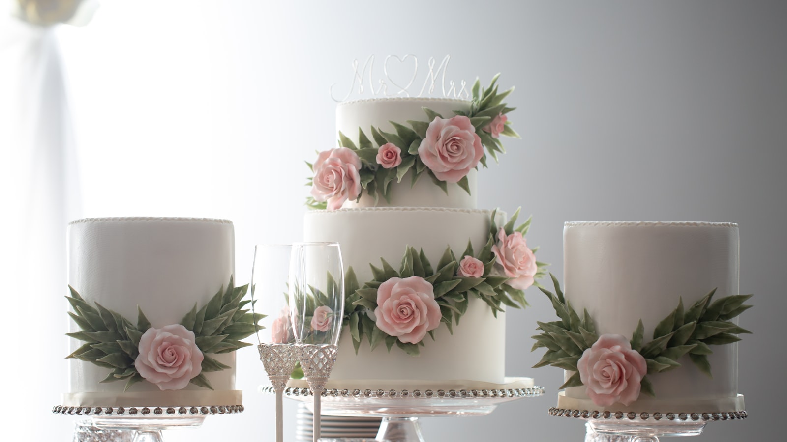 Three tiered white cakes decorated with pink roses and greenery