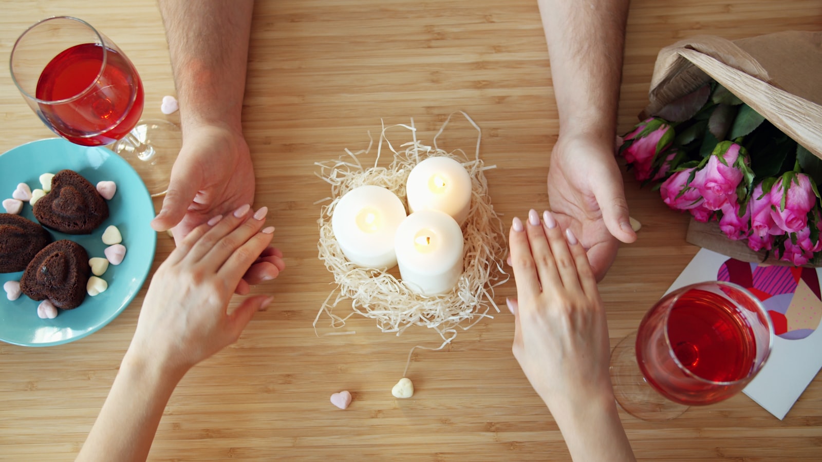 Couple holding hands over romantic dinner table with candles.